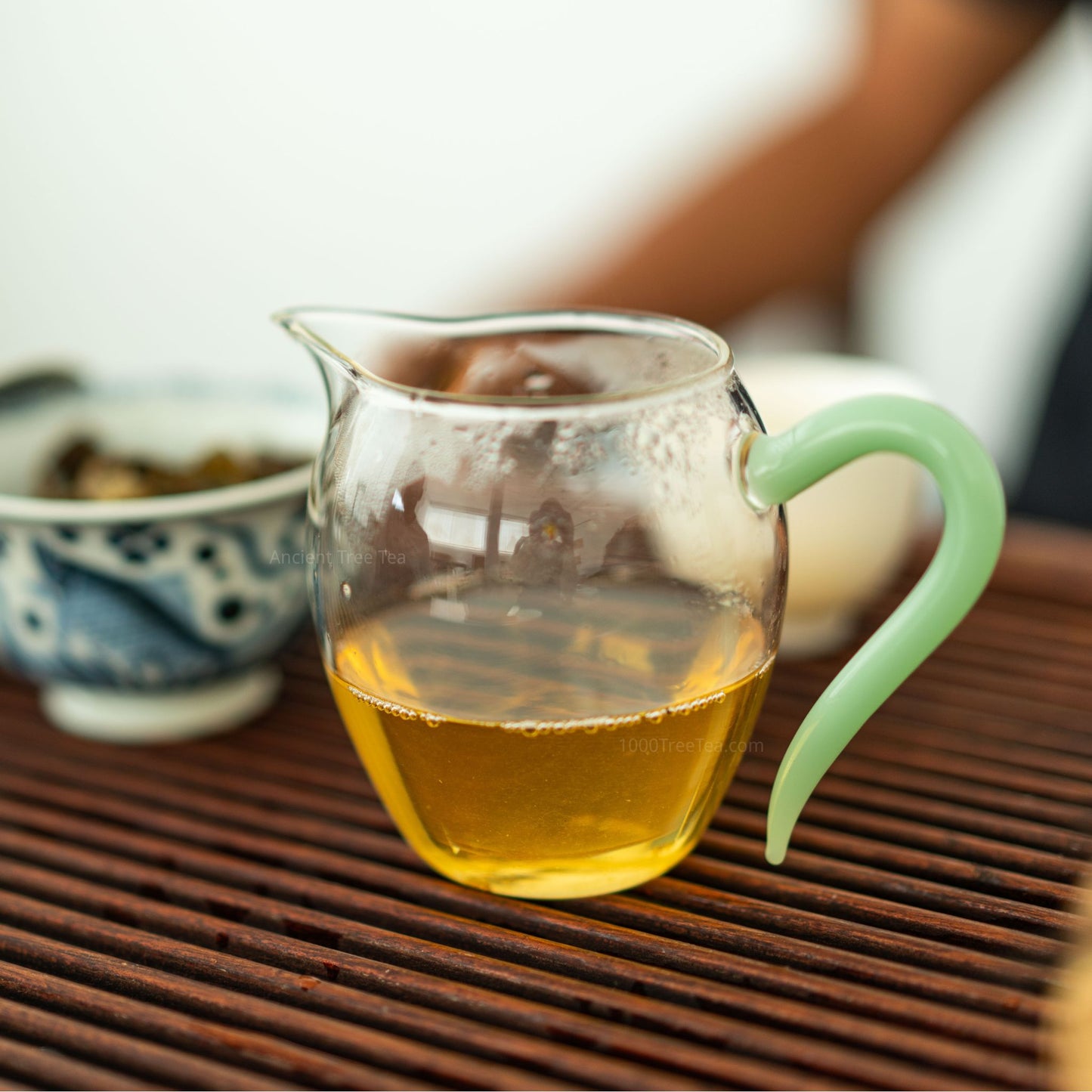 Brewed Bingdao Lao Zhai tea in glass pitcher on bamboo tea table
