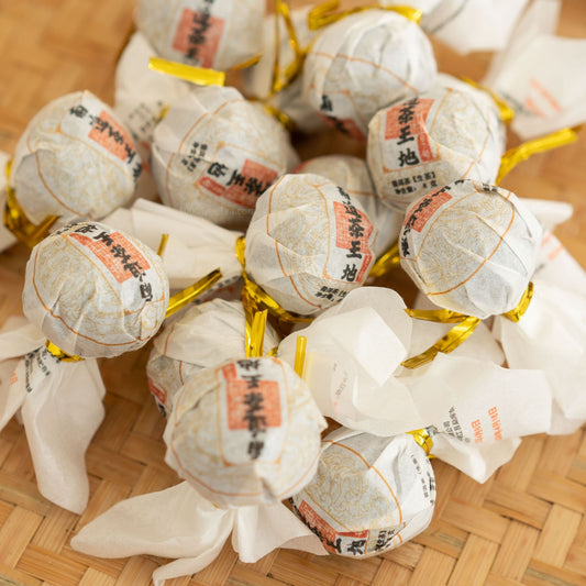 Group of individually wrapped Nanpo Dragon Ball Pu’er teas on bamboo mat